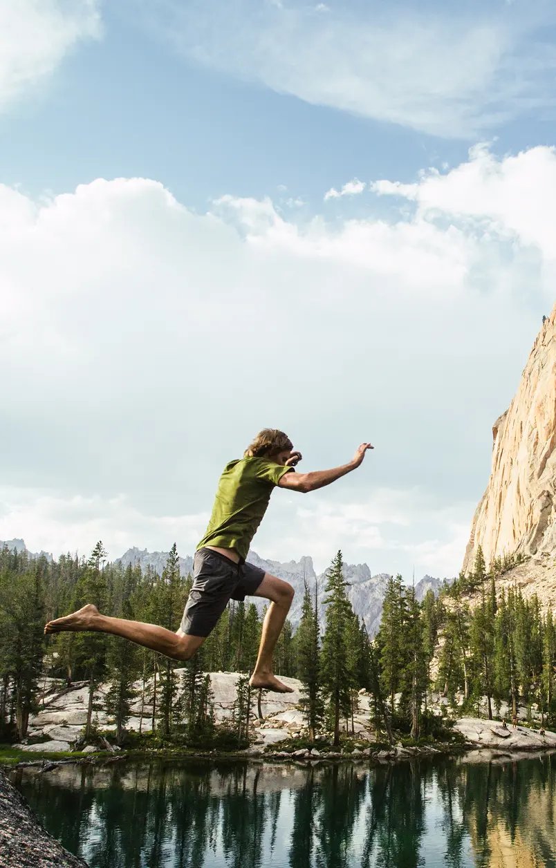 A hiker leaping across granite boulders above an alpine lake in the Idaho backcountry